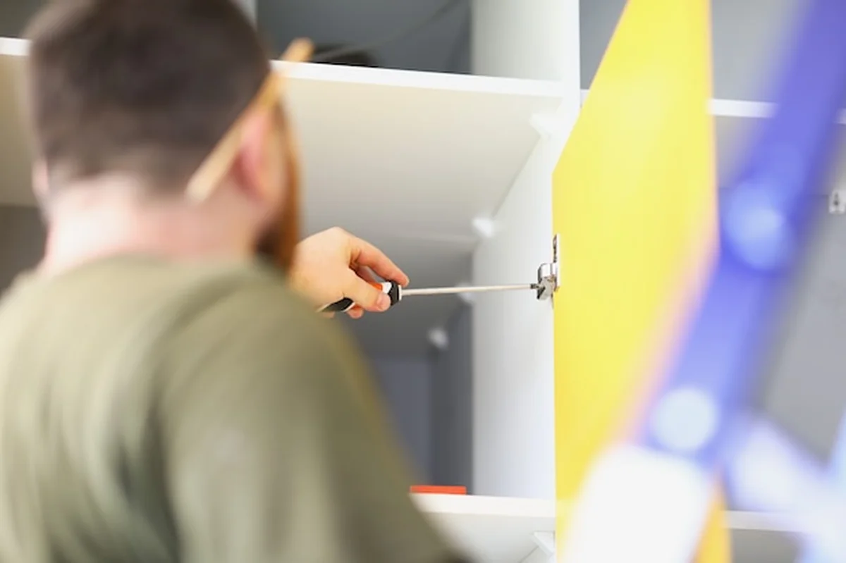 Mężczyzna stolarz dokręca uchwyt śrubokrętem w szafce wiszącej