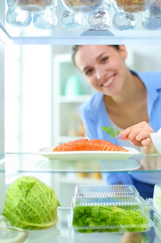 Kobieta przy otwartej lodówce z warzywami i owocami