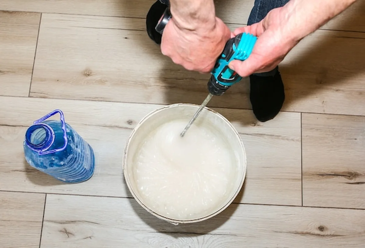 Mężczyzna miesza gęsty klej w wiadrze podczas renowacji tapety w mieszkaniu