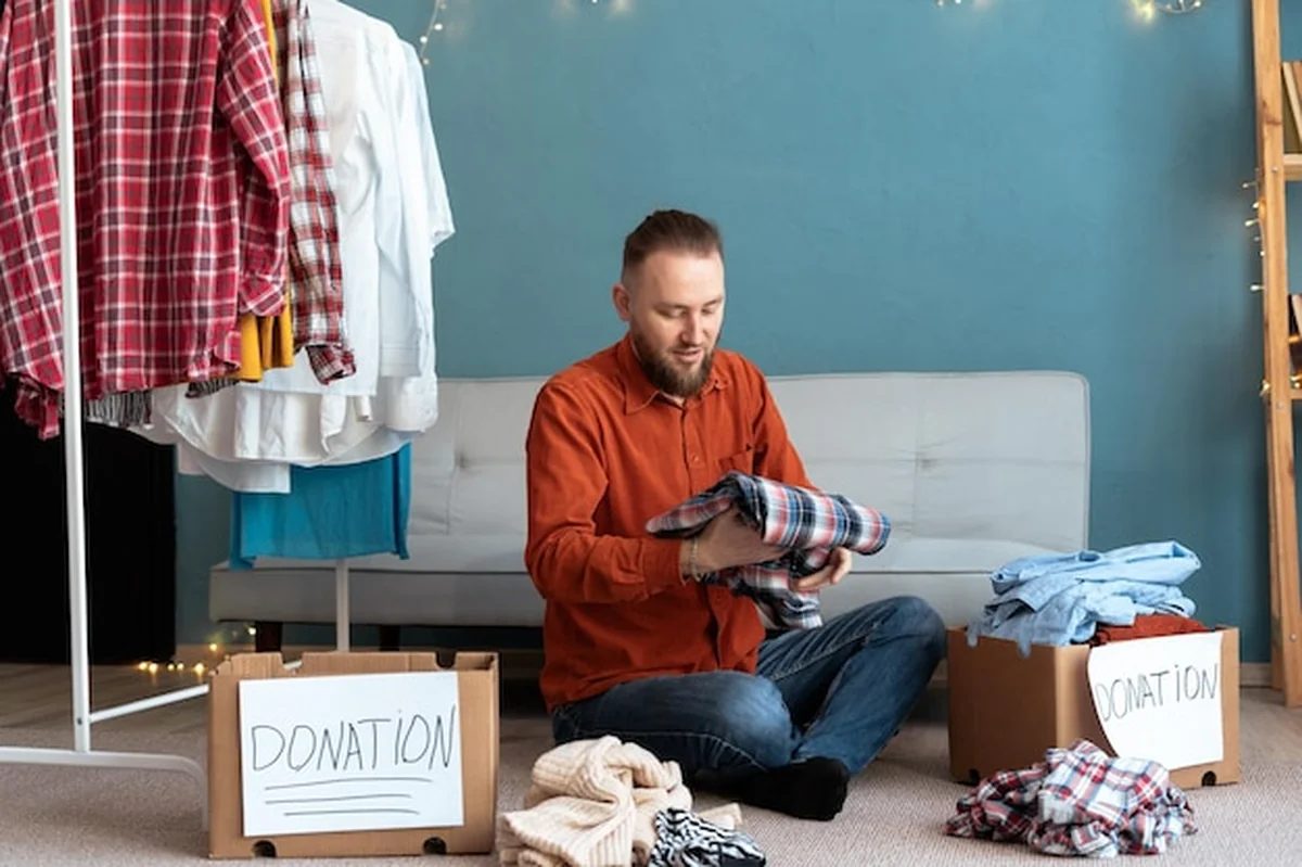 Mężczyzna składa stare ubrania do skrzynki z darowiznami na podłodze w domu