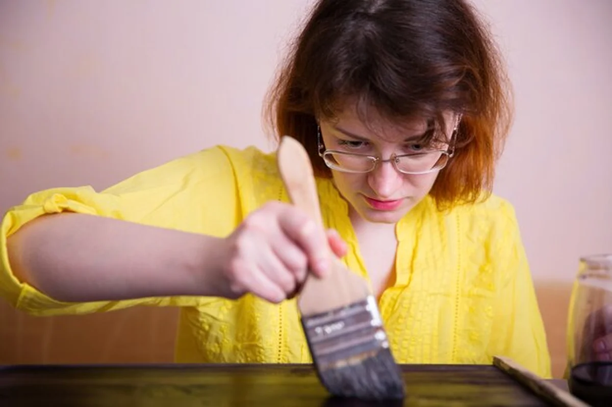 Kobieta maluje drewno na ciemny kolor