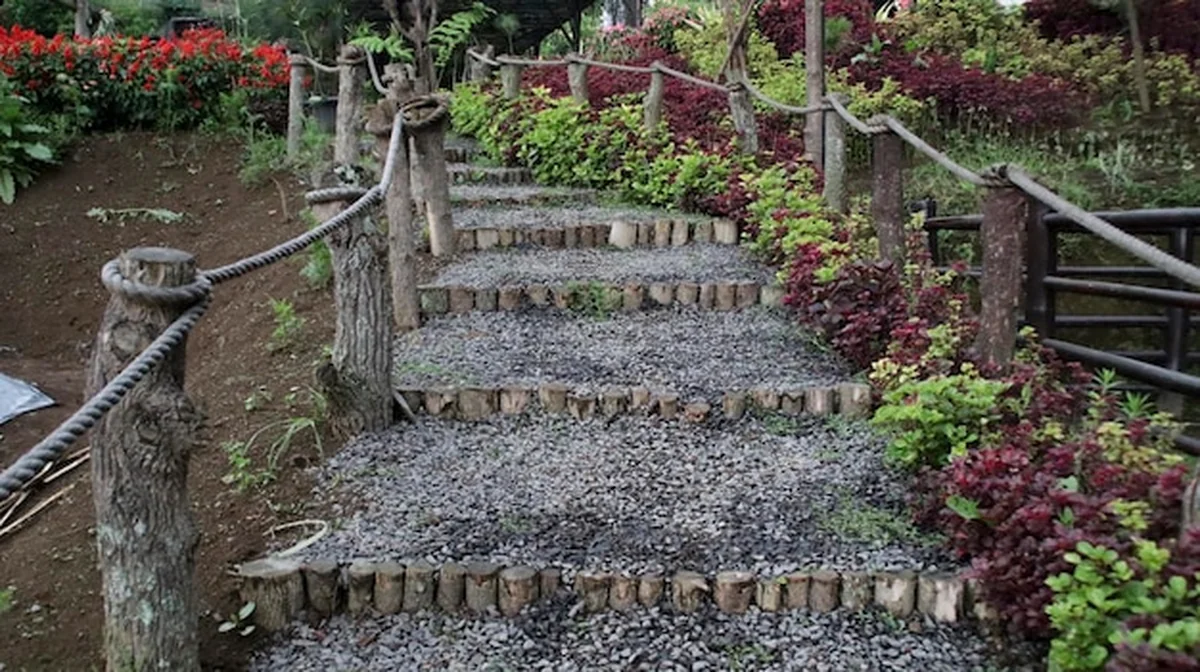 Ścieżka ogrodowa z drewnianymi schodami i poręczami z liny otoczona zielenią i kwiatami w spokojnym otoczeniu na skarpie