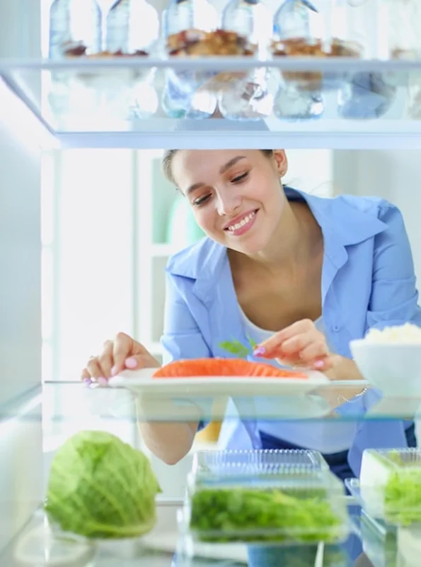 Kobieta przy otwartej lodówce pełnej zdrowych warzyw i owoców