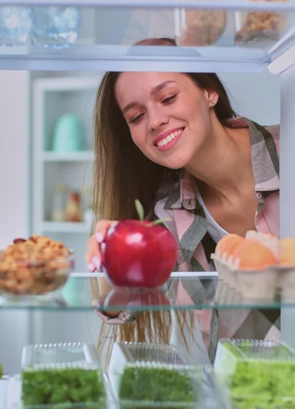 Kobieta przy otwartej lodówce z warzywami i owocami