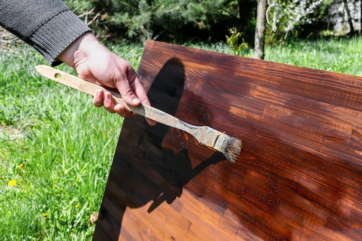 Mężczyzna maluje drewniany stół pędzlem farbą olejną