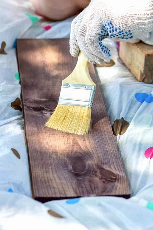 Dłoń w rękawiczce malująca drewnianą deskę pędzlem