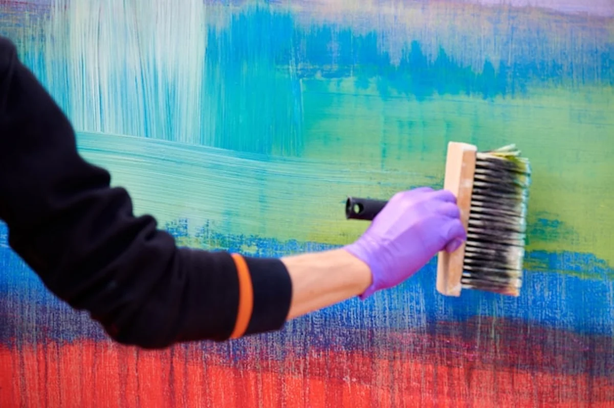 Kobieta malarz trzymająca pędzel, obraz olejny na kolorowym płótnie z szerokimi pociągnięciami pędzla