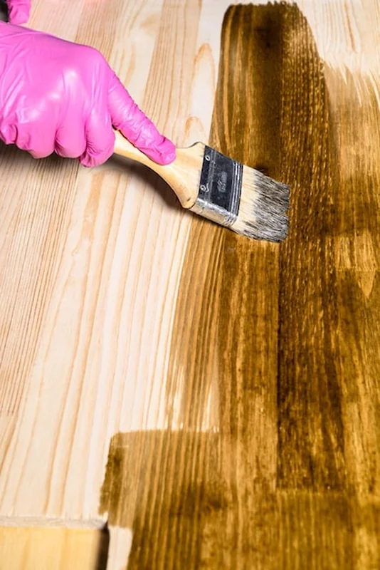 Dłoń w rękawiczce nakłada bejcę na drewnianą deskę